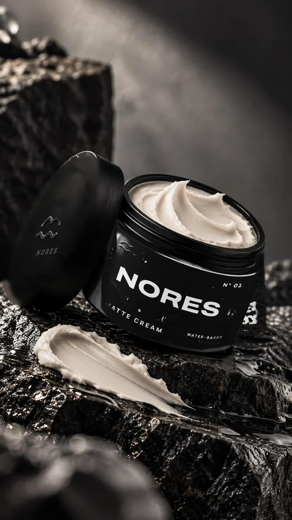 Open NORES jar on wet black rock with a swipe of cream